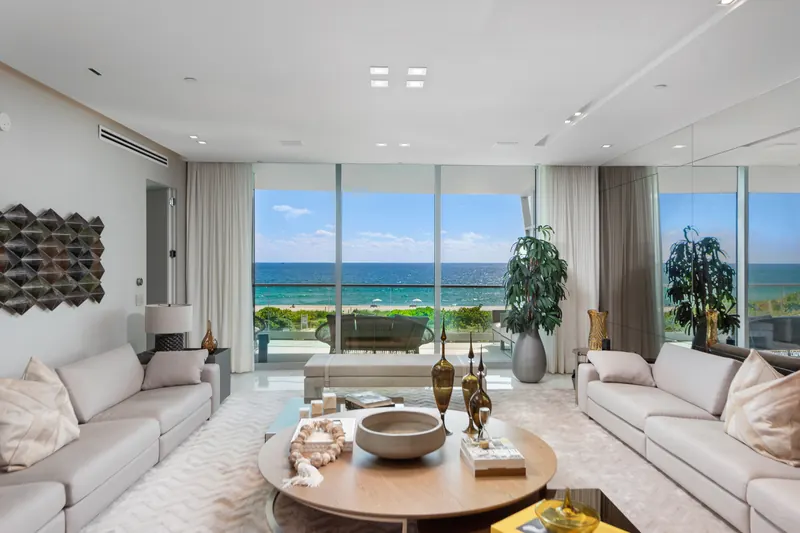 Bright living room with white sofas and floor-to-ceiling windows facing the ocean